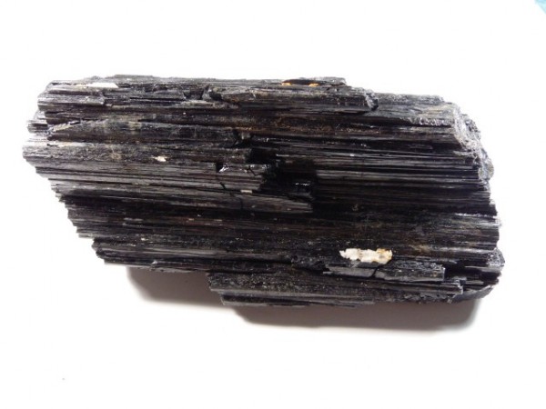 Czarny, podłużny kryształ turmalinu na białym tle.