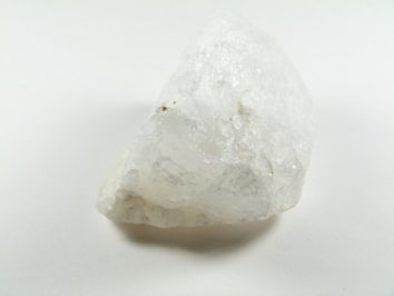 Biały, nieregularny kawałek kwarcu leży na jasnym tle.