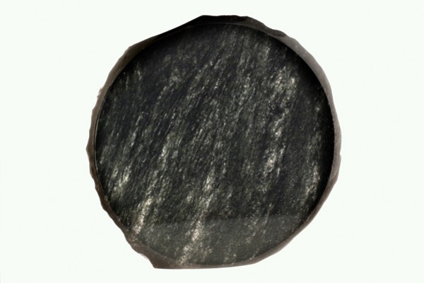 Okrągły, czarny kawałek łupka na jasnym tle, widoczna struktura kamienia.