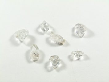 Diament Herkimer - kamień naturalny surowy nieszlifowany. Siedem surowych diamentów leży na białym tle.
