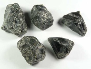 Pięć surowych czarnych kamieni leży na białym tle.