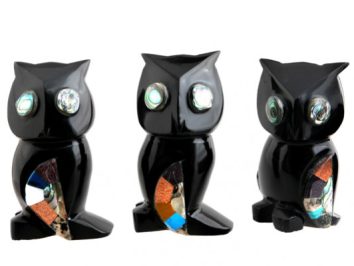 Trzy czarne figurki sów z dużymi oczami i kolorowymi wstawkami na brzuchu.