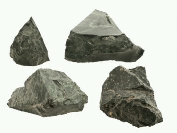 Cztery surowe, zielonkawe bryły serpentynitu na białym tle.