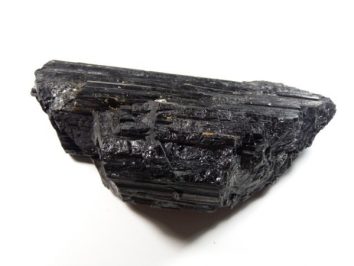 Czarny kryształ turmalinu o błyszczącej, prążkowanej powierzchni na białym tle.