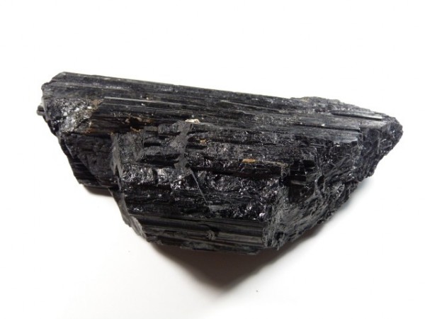 Czarny kryształ turmalinu o błyszczącej, prążkowanej powierzchni na białym tle.