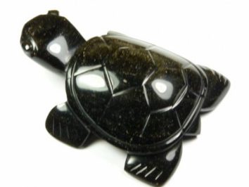 Czarna figurka żółwia wykonana z kamienia, widok z góry na białym tle.