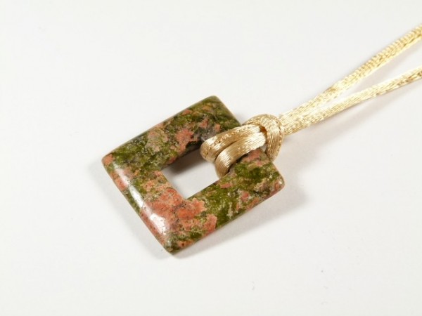 Kwadratowy wisiorek z kamienia w odcieniach zieleni i różu na beżowym sznurku.