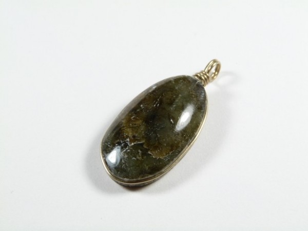 Owalny wisiorek z ciemnozielonym kamieniem na jasnym tle.