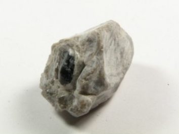 Łza Apacza - kamień naturalny, surowy, nieszlifowany. Szary, nieregularny kamień z ciemniejszą wstawką na białym tle.
