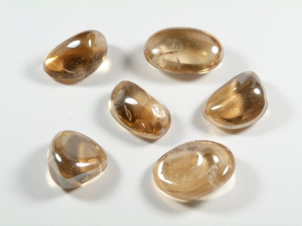 Kwarc tangerine aura - kamień gładzony, polerowany, szlifowany i bębnowany w formie otoczaka. Sześć polerowanych, jasnobrązowych kamieni leży na białym tle.