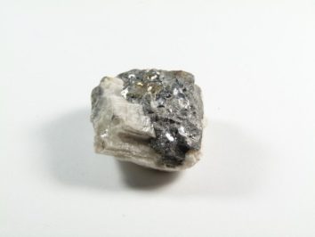 Skutterudyt - kamień naturalny, surowy, nieszlifowany. Szaro-biały minerał z połyskującymi fragmentami na białym tle.