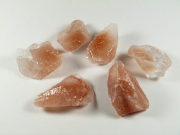 Sześć kawałków różowej soli himalajskiej leży na białym tle.