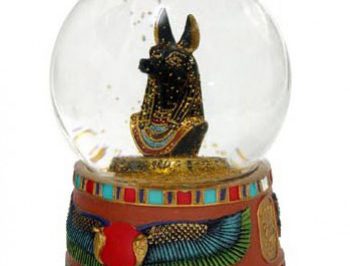 Szklana kula z figurką egipskiego boga Anubisa na ozdobnej podstawie.