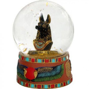 Szklana kula z figurką egipskiego boga Anubisa na ozdobnej podstawie.