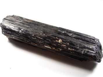 Czarny kryształ turmalinu o podłużnym, prążkowanym kształcie na białym tle.