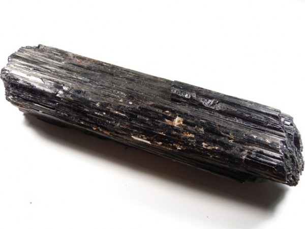 Czarny kryształ turmalinu o podłużnym, prążkowanym kształcie na białym tle.