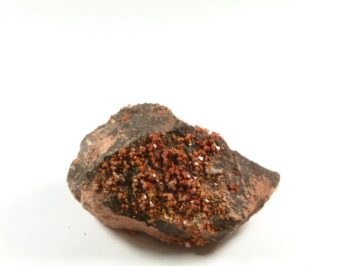 Kawałek skały z brązowymi i czerwonymi kryształami wystawiony na białym tle.