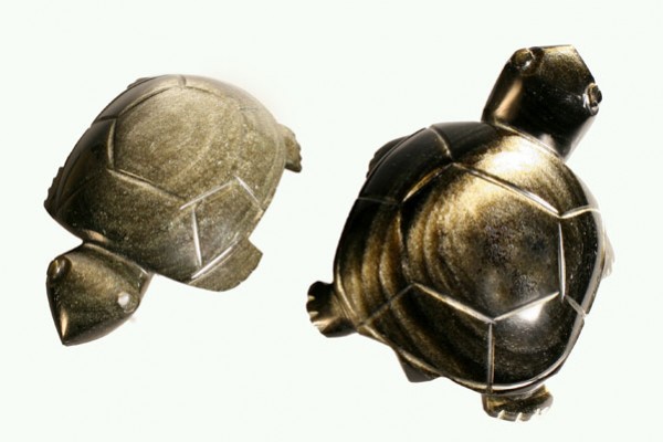 Dwa figurki żółwi z metalu ustawione na białym tle.