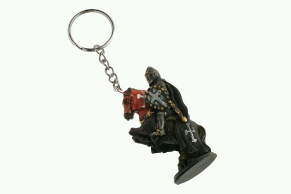 Breloczek w kształcie rycerza na koniu w ciemnej zbroi i pelerynie z krzyżem.