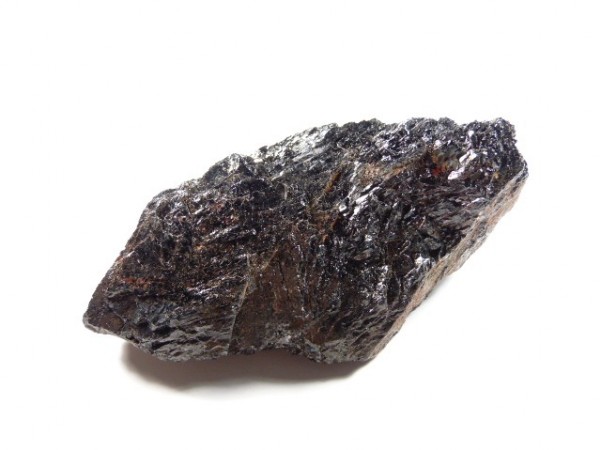 Czarny, błyszczący kawałek surowego minerału na białym tle.