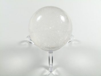 Kula kryształ górski na podstawce. Przezroczysta kula kryształu górskiego stoi na przezroczystym stojaku na białym tle.