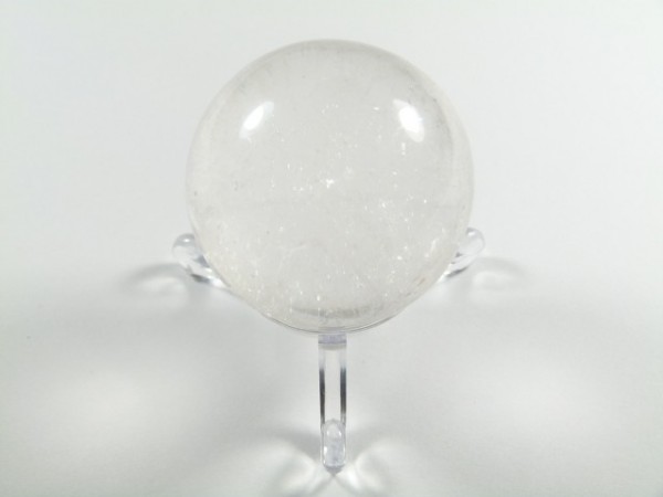 Kula kryształ górski na podstawce. Przezroczysta kula kryształu górskiego stoi na przezroczystym stojaku na białym tle.