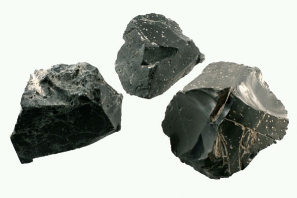 Trzy czarne bryły obsydianu na jasnym tle.