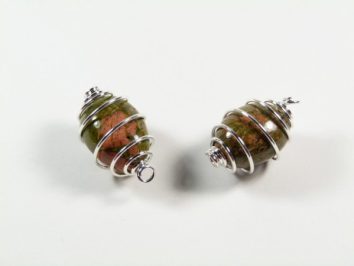 Unakit gładzony w spirali - wisiorek na sznureczku. Dwa kamienie owinięte srebrnym drutem leżące na białym tle.