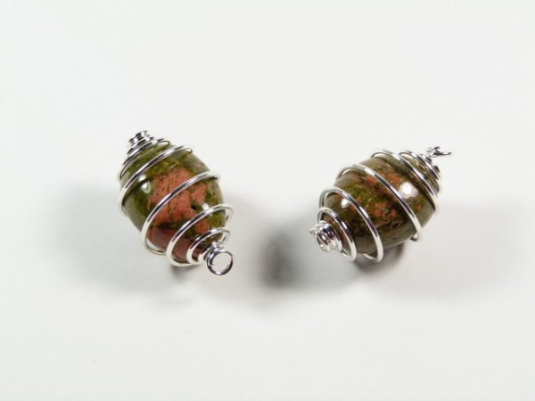 Unakit gładzony w spirali - wisiorek na sznureczku. Dwa kamienie owinięte srebrnym drutem leżące na białym tle.