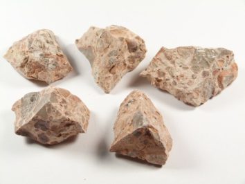 Pięć kawałków różowawego kamienia na białym tle.