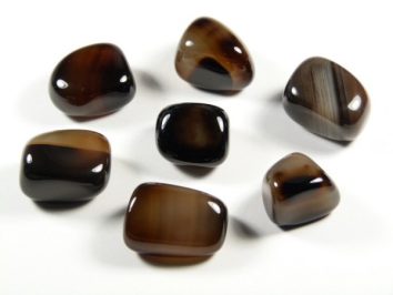 Onyks - kamień gładzony, polerowany, szlifowany i bębnowany w formie otoczaka. Siedem polerowanych kamieni na białym tle.