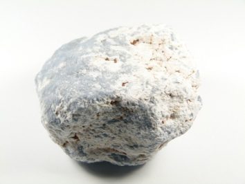 Szaro-biały, chropowaty kamień na białym tle, widoczna nierówna powierzchnia.