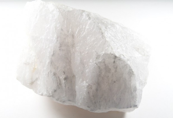 Biały, matowy fragment minerału kwarcu na jasnym tle.