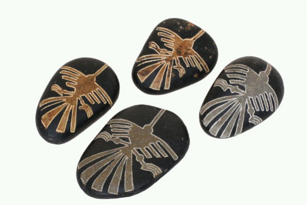 Cztery czarne kamienie z wygrawerowanym wzorem ptaka w stylu rysunków z Nazca.