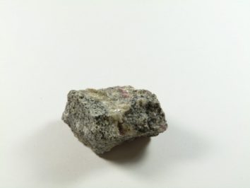 Szary kamień o nieregularnym kształcie leży na białym tle.