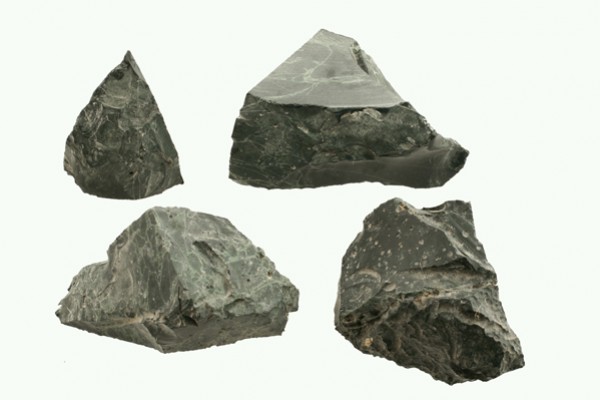 Cztery surowe, ciemnozielone kawałki skały serpentynitu na jasnym tle.