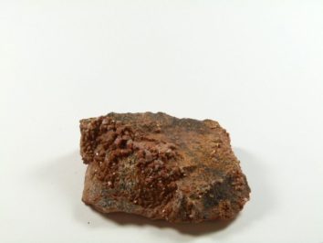 Wanadynit - kamień naturalny, surowy, nieszlifowany. Bryła brązowego wanadynitu na białym tle, powierzchnia częściowo chropowata.