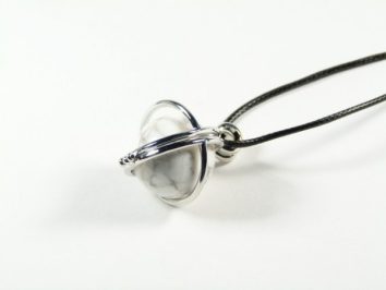 Srebrny wisiorek z marmurkową kulką zawieszony na czarnym rzemieniu, na białym tle.