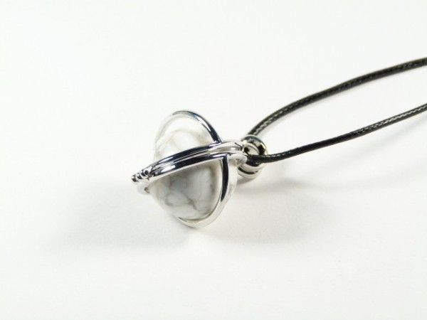 Srebrny wisiorek z marmurkową kulką zawieszony na czarnym rzemieniu, na białym tle.