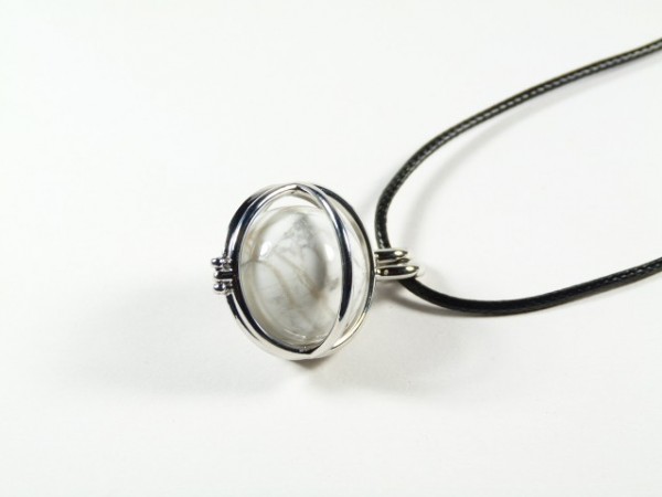 Wisiorek z białym kamieniem oprawiony w srebro na czarnym rzemyku, na białym tle.