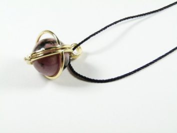Wisiorek z fioletowym kamieniem w złotej oprawie na czarnym sznurku, na białym tle.