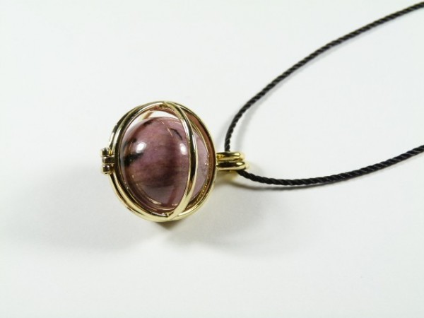 Wisior z fioletowym kamieniem w złotej oprawie na czarnym sznurku, na białym tle.