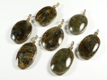 Siedem owalnych wisiorków z labradorytu z metalową zawieszką, ułożonych na białym tle.