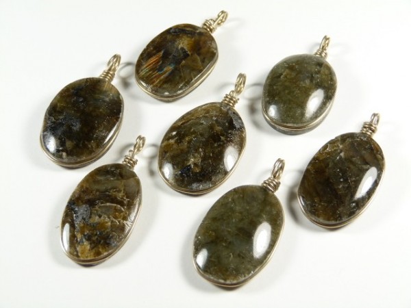 Siedem owalnych wisiorków z labradorytu z metalową zawieszką, ułożonych na białym tle.