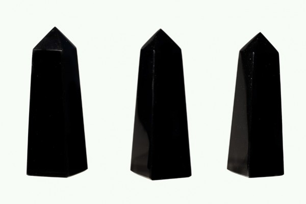 Trzy czarne, błyszczące obeliski stojące na jasnym tle.