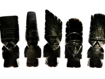 Pięć czarnych, rzeźbionych figurek przedstawiających stylizowane postacie ludzkie w pióropuszach.