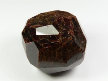 Granat almandyn okaz gładzony. Brązowy, wielościenny kryształ granatu na białym tle.