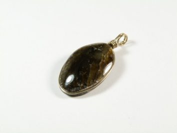 Owalny wisiorek z ciemnego kamienia w srebrnej oprawie, leżący na białym tle.