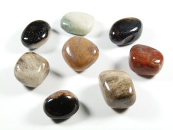 Osiem kolorowych, wygładzonych kamyków ułożonych na białym tle.