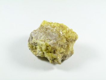 Siarka - kamień naturalny, surowy, nieszlifowany. Żółty minerał siarki na białym tle, widoczna chropowata powierzchnia kamienia.